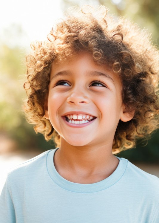 Child in blue shirt smiling outside