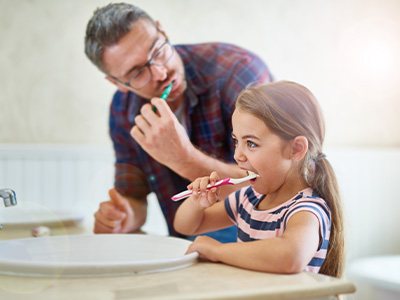 Father and daughter brushing teeth together in bathroom