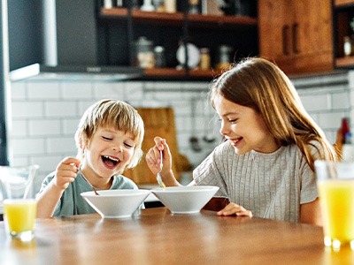 Two children smiling while eating breakfast together