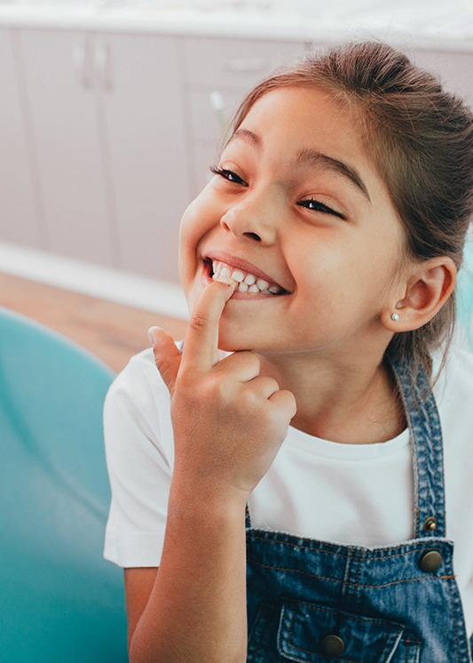 happy little girl pointing to her smile after her dental checkup and cleaning