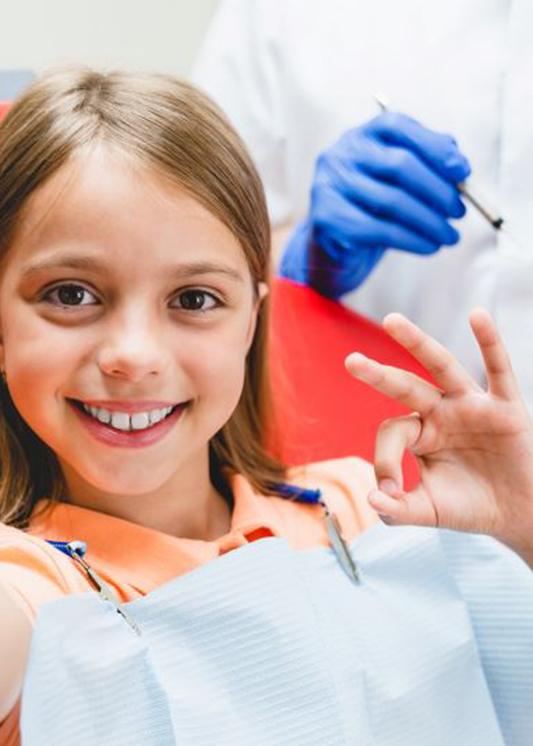 Preteen girl in dental treatment chair, making OK sign