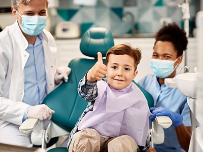 Happy little boy in dental treatment chair, making thumbs up gesture